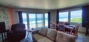 A living room with a view of the beach, a sofa, a TV, and a dining area with chairs. - Condo #208 with beautiful sunset view from your balcony overlooking the ocean (Lincoln City)