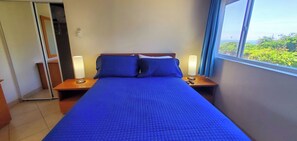 Ein Hotelzimmer mit einem großen Bett, zwei Nachttischen, einem Spiegel und einem Fenster mit Blick auf Grünflächen.