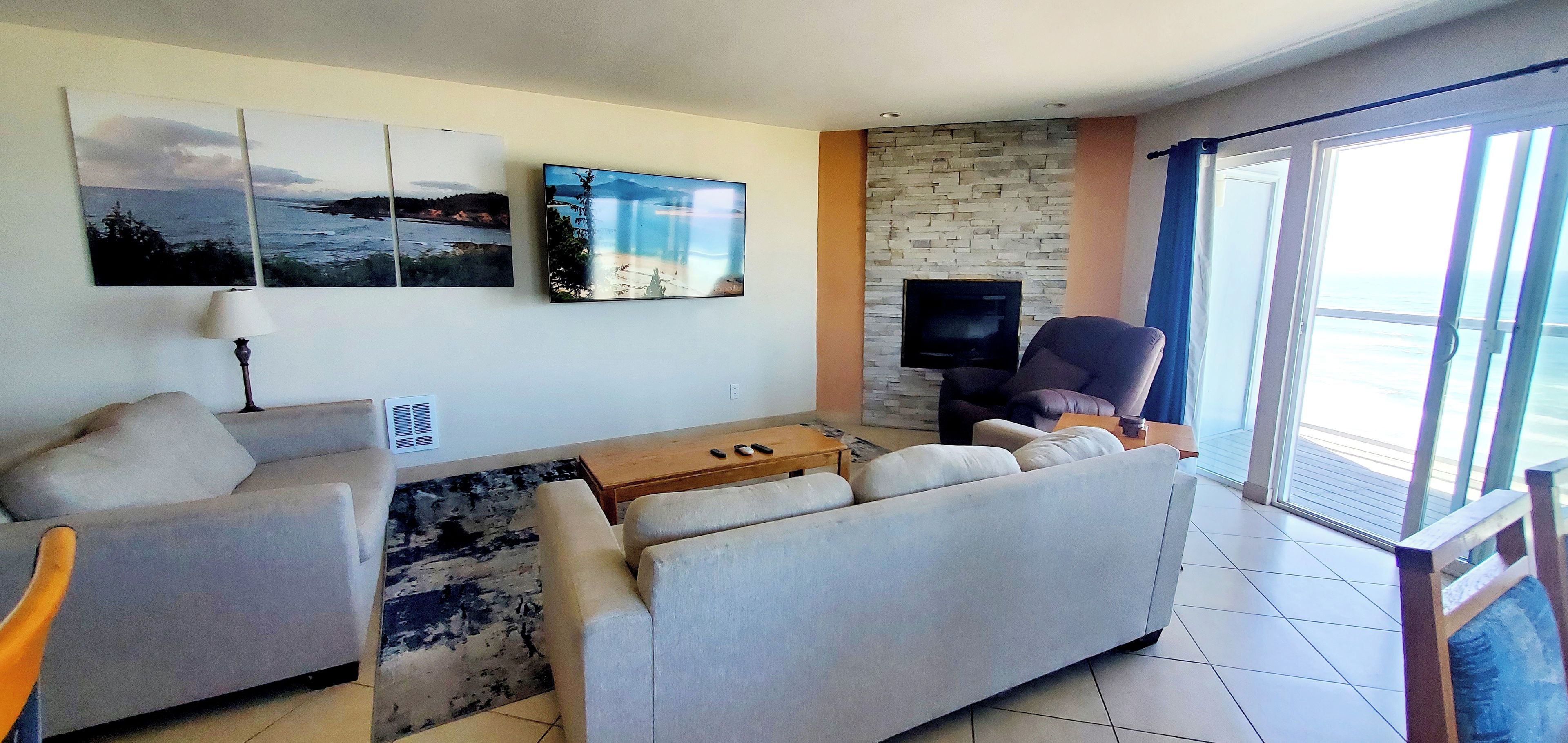 A living room with a sofa, a coffee table, and a flat-screen TV against a stone wall.