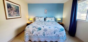 Ein Schlafzimmer mit einem Bett, zwei Nachttischen, einem gerahmten Bild und einem Fenster mit Vorhängen.