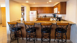 A kitchen with wooden cabinets, a white refrigerator, a stove, and four bar stools. - Condo #308 with beautiful sunset view from your balcony overlooking the ocean (Lincoln City)