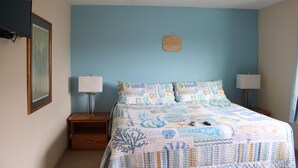 A bedroom with a bed, two bedside tables, a nightstand, a wall-mounted lamp, and a framed picture. - Condo #308 with beautiful sunset view from your balcony overlooking the ocean (Lincoln City)