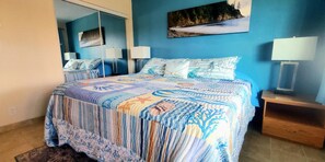 Un dormitorio con cama, mesita de noche, espejo y un cuadro en la pared.