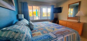 Une chambre à coucher avec un lit, une télévision, une commode et une fenêtre avec des rideaux.