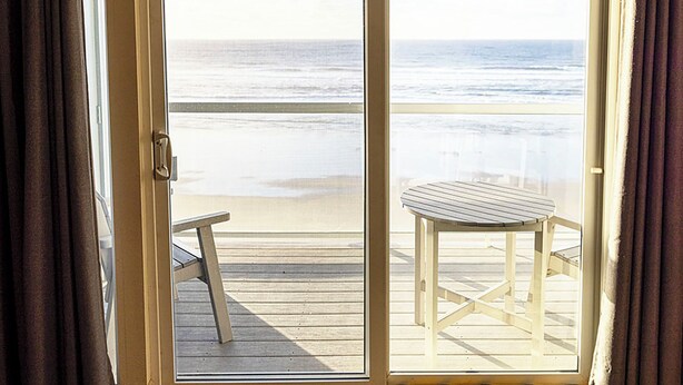 Ein Zimmer mit Blick auf den Strand, einer Holzterrasse und einem Tisch.