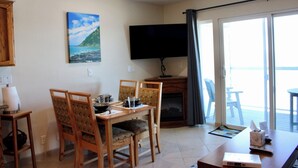 Ein Essbereich mit Holzkästen und einem Tisch, einem an der Wand montierten Fernseher und Blick ins Freie durch eine Schiebetür.