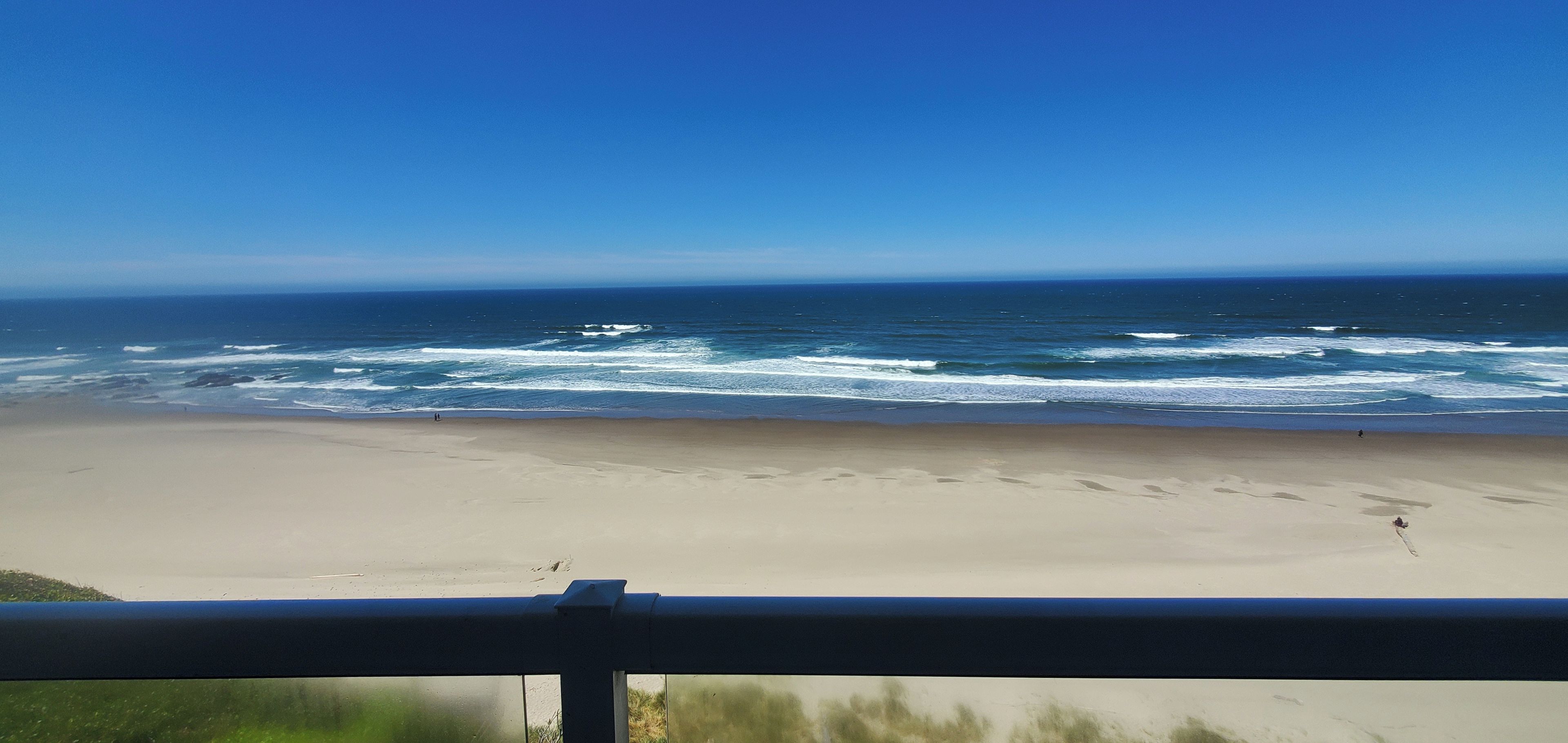 A beach with waves, a clear sky, and a railing in the foreground.