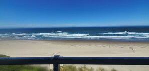 Una playa con olas, cielo despejado y una baranda al frente.
