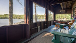 A cabin with a view of a lake, wooden deck, and a table with chairs. - Quintessential Maine Lake House, 280Ft of Waterfront, near Acadia & Bar Harbor (Dedham)
