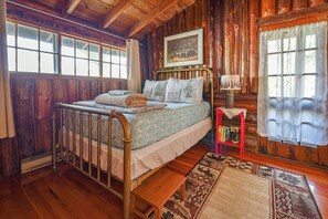 A wooden cabin bedroom with a bed, a small table, and a window with curtains.