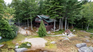 A cabin surrounded by trees, a small outdoor seating area, and a pond. - Quintessential Maine Lake House, 280Ft of Waterfront, near Acadia & Bar Harbor (Dedham)
