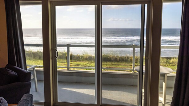 Een kamer met een schuifglazen deur naar een balkon met uitzicht op zee.