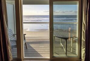 A room with a view of the beach, a sliding glass door, a small table, and a bench. - Condo #204 with beautiful sunset view from your balcony overlooking the ocean (Lincoln City)