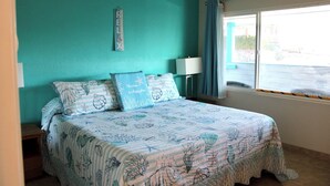 A bedroom with a bed, a nightstand, a lamp, a window with curtains, and a wall decoration. - Condo #204 with beautiful sunset view from your balcony overlooking the ocean (Lincoln City)