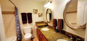 Ein Badezimmer mit Toilette, Waschbecken und Dusche. Handtücher und ein Spiegel sind vorhanden.