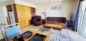 A living room with a sofa, armchair, coffee table, and a bookshelf. - Condo #108 with beautiful sunset view from your balcony overlooking the ocean (Lincoln City)
