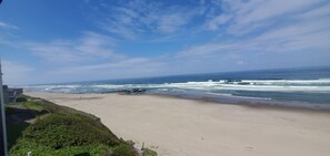 A beach with waves, a clear sky, and a building in the background. - Condo #108 with beautiful sunset view from your balcony overlooking the ocean (Lincoln City)