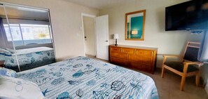Una habitación de hotel con una cama, un aparador de madera, una silla, un televisor y una puerta.