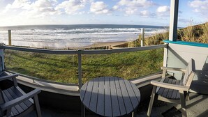Ein Balkon mit Meerblick, ausgestattet mit zwei Adirondack-Stühlen und einem kleinen runden Tisch.