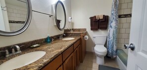 Une salle de bain avec deux lavabos, des toilettes, un rideau de douche et un porte-serviettes.