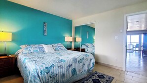Une chambre à coucher comprenant un lit, deux tables de chevet, une commode, un miroir et une vue sur le balcon.