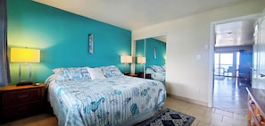 Une chambre à coucher comprenant un lit, deux tables de chevet, une commode, un miroir et une vue sur le balcon.