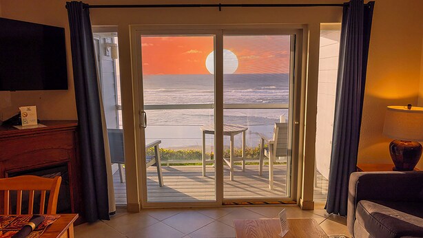 Ein Zimmer mit einer großen SchiebeglasTür, die auf einen Balkon mit Meerblick und Sonnenuntergang führt.