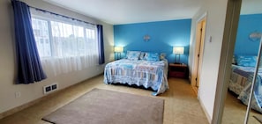 Une chambre à coucher avec un lit, deux lampes de chevet, une fenêtre avec des rideaux, un miroir sur le mur et une porte donnant sur une autre pièce.