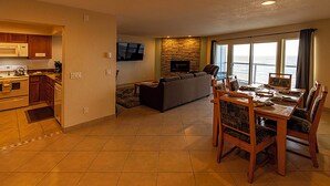 A modern living room with a stone fireplace, a dining area with wooden furniture, and a kitchen with wooden cabinets and a microwave. - Condo #307 with beautiful sunset view from your balcony overlooking the ocean (Lincoln City)