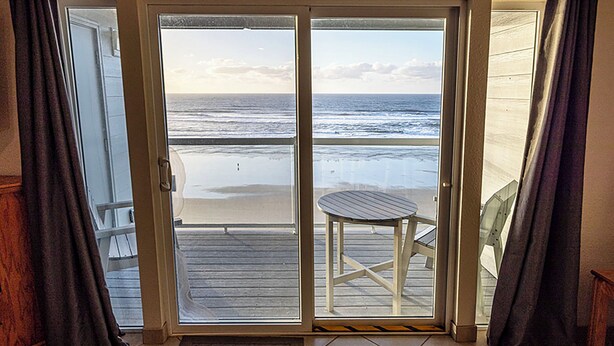 A room with a sliding glass door leading to a balcony with a view of the beach. - Condo #206 with beautiful sunset view from your balcony overlooking the ocean (Lincoln City)