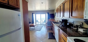 A kitchen with wooden cabinets, a refrigerator, a coffee maker, and a dining area with a table and chairs. - Condo #203 with beautiful sunset view from your balcony overlooking the ocean (Lincoln City)