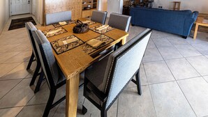 A dining area with a wooden table and chairs, a kitchen in the background, and a blue sofa. - Condo #207 with beautiful sunset view from your balcony overlooking the ocean (Lincoln City)