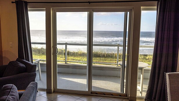 A room with a large sliding glass door leading to a balcony with a view of the ocean. - Condo #207 with beautiful sunset view from your balcony overlooking the ocean (Lincoln City)
