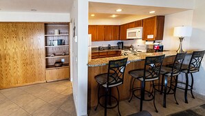 A kitchen with wooden cabinets, a microwave, a stove, and a bar area with four stools. - Condo #207 with beautiful sunset view from your balcony overlooking the ocean (Lincoln City)