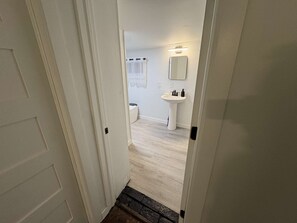 A narrow hallway leading to a bathroom with a white sink and a mirror. - Temple Apartment Unit 1 2 bedrooms (Philadelphia)