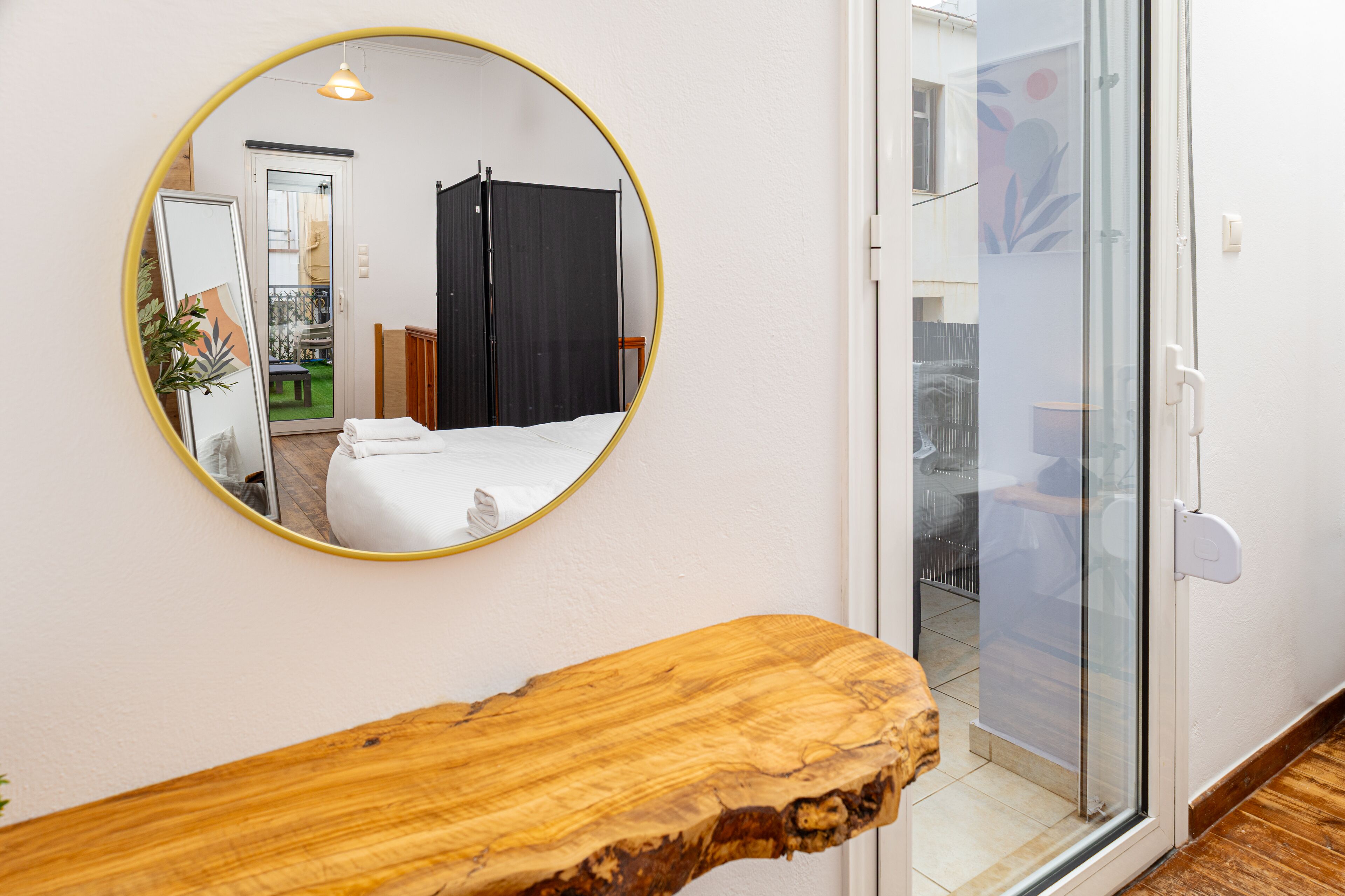 A room with a wooden console table, a round mirror on the wall, and a sliding glass door leading to a balcony.