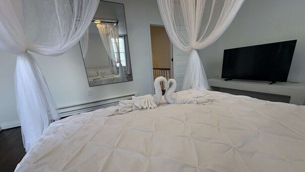 A hotel room with a large bed, white curtains, a flat-screen TV, and a mirror on the wall. - Temple Apartment Unit 2 1 bedroom (Philadelphia)