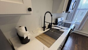 A modern kitchen with a white marble countertop, a wooden backsplash, a black faucet, and a window with blinds. - Temple Apartment Unit 2 1 bedroom (Philadelphia)