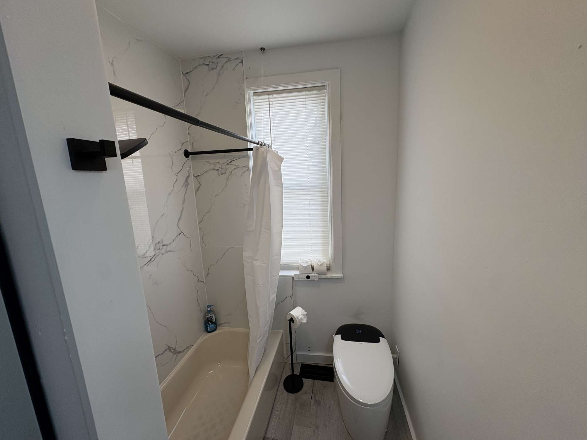 Ein Badezimmer mit Badewanne, Toilette und einem Fenster mit Jalousien.