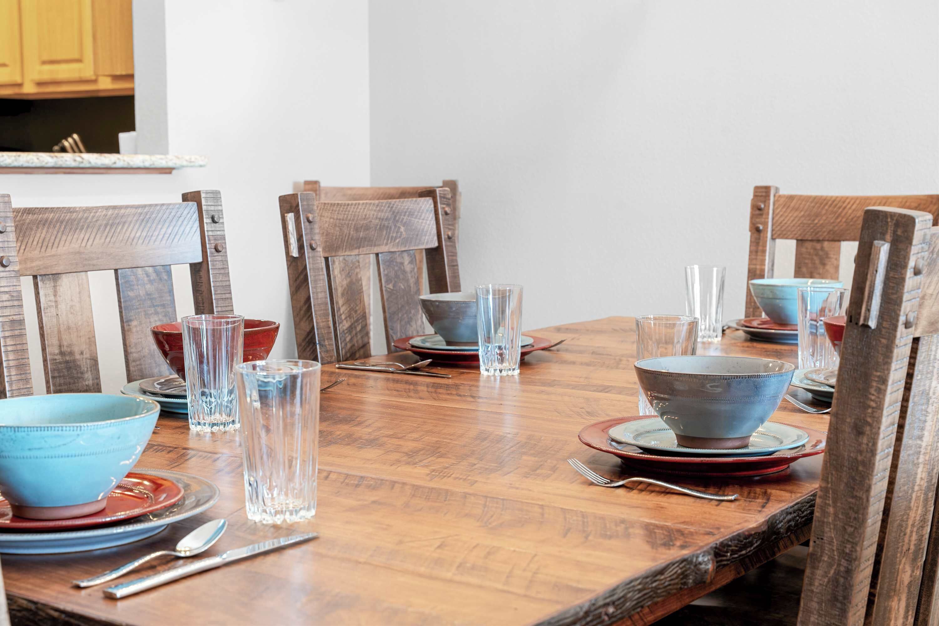 Une table de salle à manger en bois, mise avec des bols bleus, des assiettes rouges et des verres transparents.