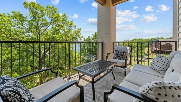 Un balcon abrité, doté de mobilier d’extérieur, d’une table et offrant une vue sur les arbres et les bâtiments.