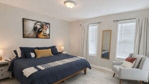 A bedroom with a large bed, bedside tables, a chair, a painting, and two windows with curtains. - Music Weekend in Woodstock| Madlife|Lamplighter|Am (Woodstock)