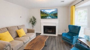 A living room with a fireplace, a sofa, a coffee table, and a blue armchair. - Music Weekend in Woodstock| Madlife|Lamplighter|Am (Woodstock)