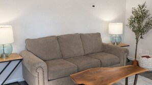 A living room with a beige sofa, two side tables with lamps, a wooden coffee table, and a potted plant. - Music Weekend in Woodstock| Madlife|Lamplighter|Am (Woodstock)