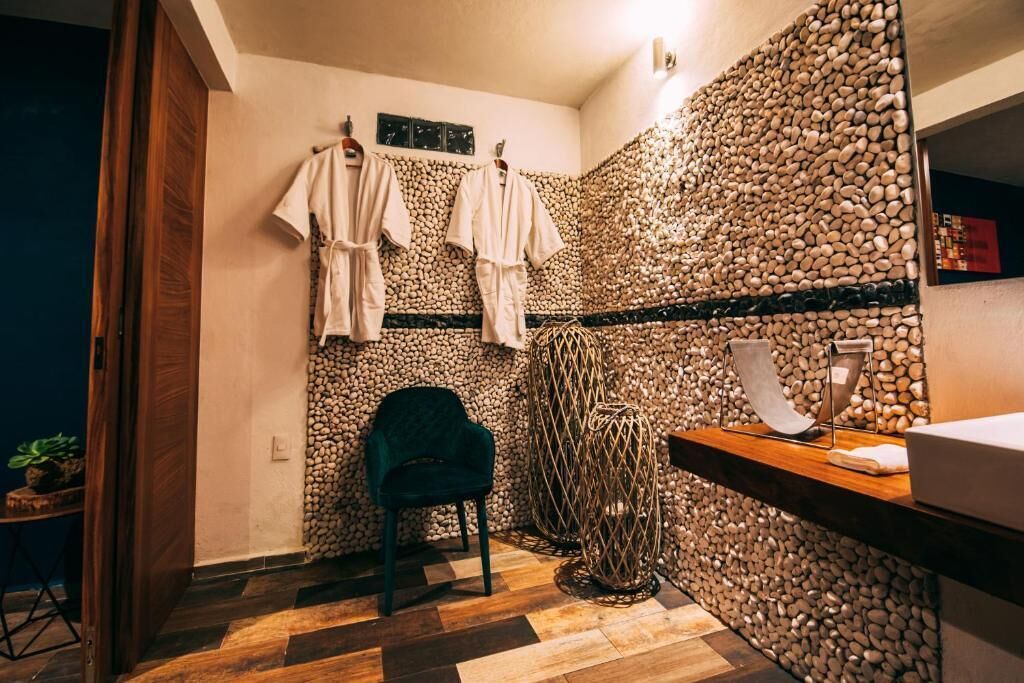 A bathroom with a stone wall, a wooden bench, a chair, and a towel rack.