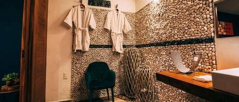 A bathroom with a stone wall, a wooden bench, a chair, and a towel rack.