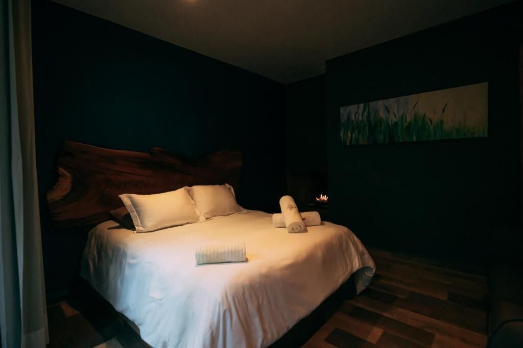 Una cama bien hecha con sábanas y almohadas blancas, un cabecero de madera y un cuadro de hierba en la pared.
