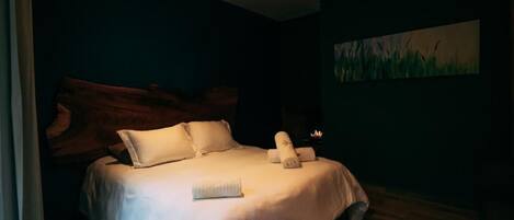 Una cama bien hecha con sábanas y almohadas blancas, un cabecero de madera y un cuadro de hierba en la pared.