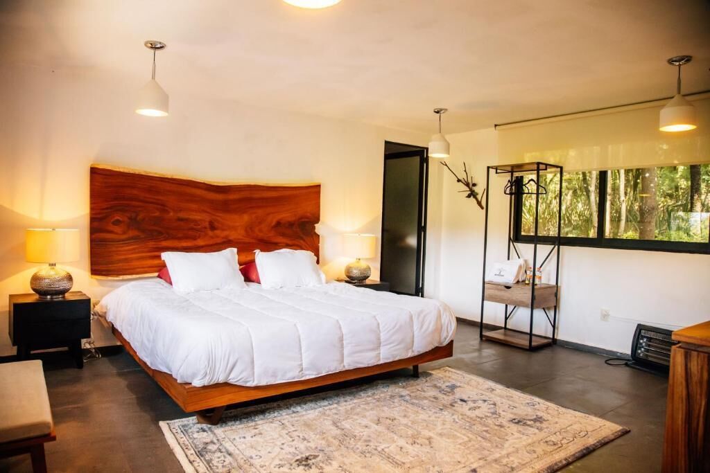 Un dormitorio moderno con una cama grande, lámparas de noche, un cabecero de madera, una lámpara de pie y vistas a zonas verdes a través de la ventana.