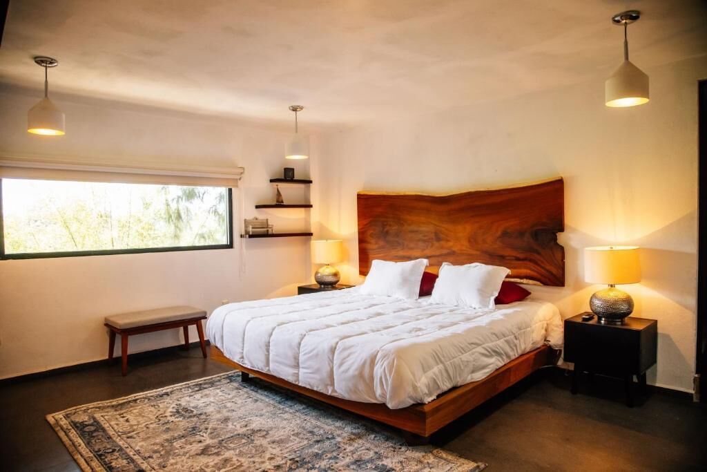 Een slaapkamer met een groot bed, nachtkastjes, een bankje en een raam met uitzicht.